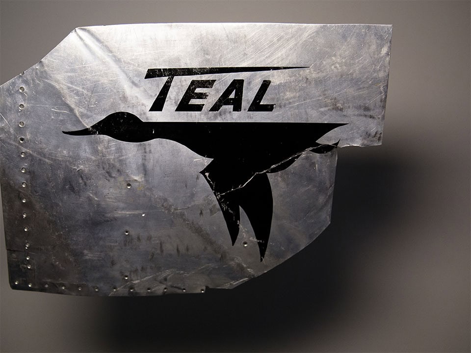 Piece of aluminum with "Teal" printed and a silhouetted of a duck in flight.
