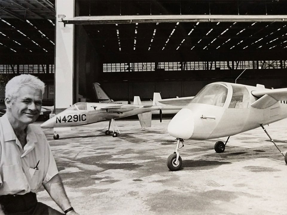 Lesher posing in front of his Nomad and Teal planes in front of a hangar.