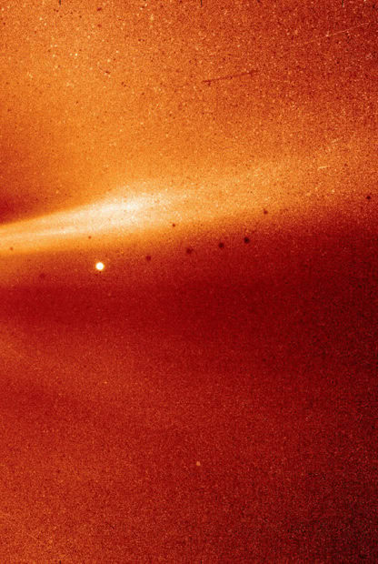 A stream of bright white and yellow particles against a red background in space.