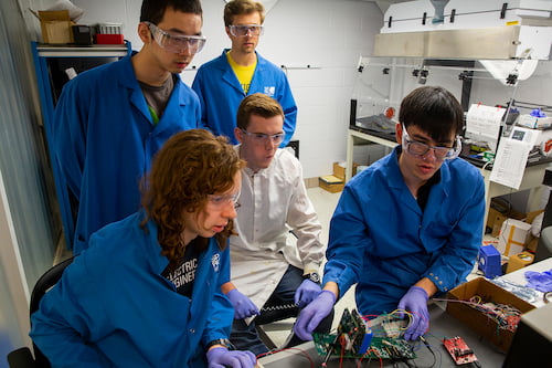 Five people working in a lab wearing blue jackets.
