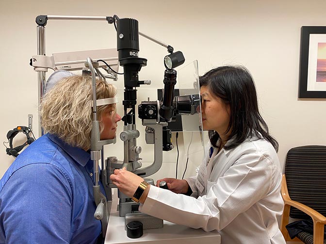 Doctor examines patients eyes via equipment fitted with a plastic protective shield