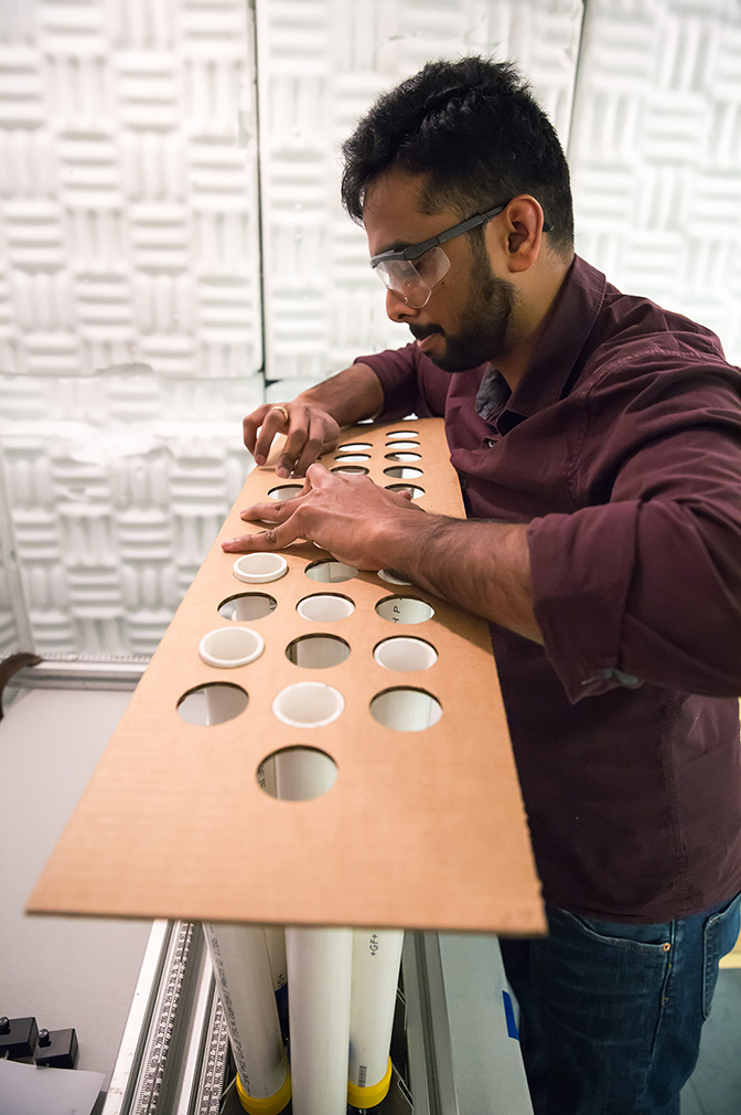 an image of research assistant manoj thota placing a lattice pattern cutout over the cylindrical rods to hold them in place temporarly to keep the rods evenly spaced