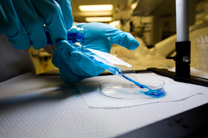 an image of graduate student pouring viscous lubricants onto a flexible plastic slide with a superomniphobic coating