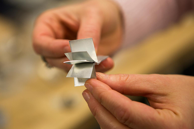 Hands holding several small sheets of metal.