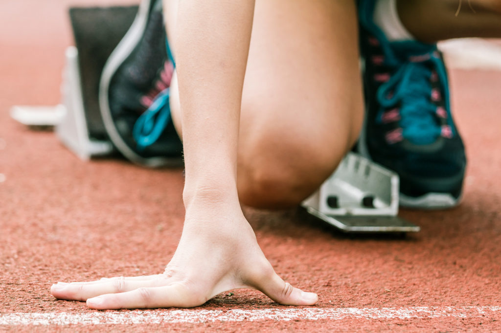 Person's hand while they kneel on ground at the starting line of a race