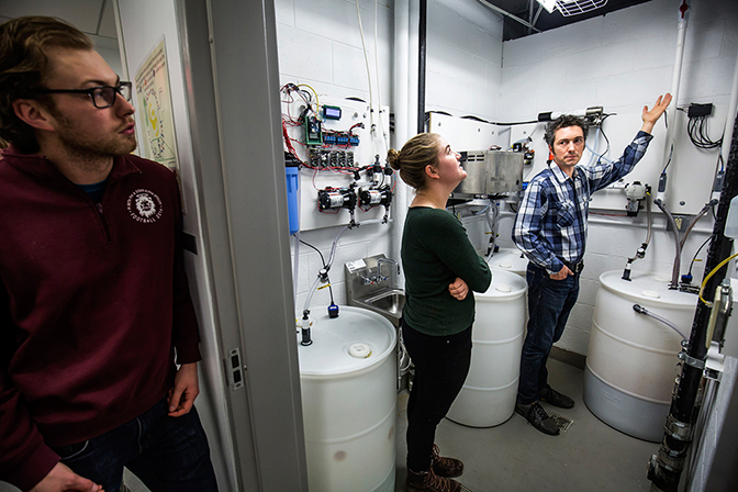 Two people in a room with large tanks on the floor and pipes.