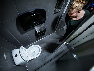 A woman peering into a public restroom stall.