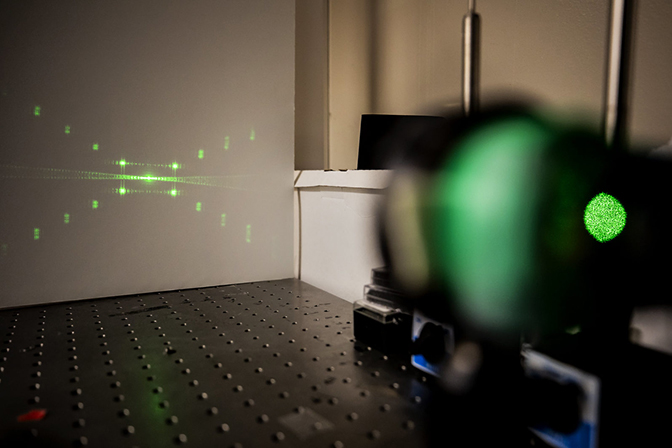 A device shines a green X-shaped light on a white wall.