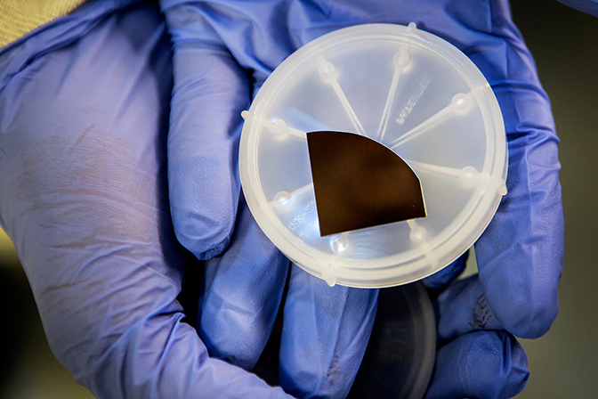 A pair of gloved hands holding a dish with a small chip in it.