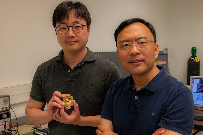 Two men facing the camera, one of whom is holding a small chip.