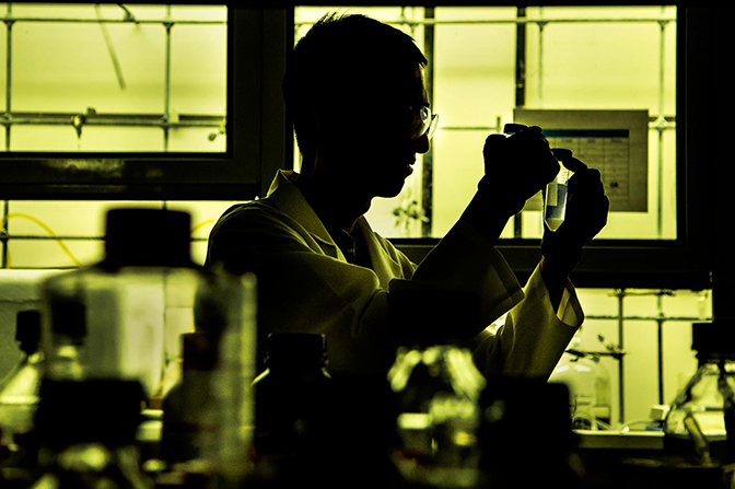 A man in a lab holding up a test tube of liquid.