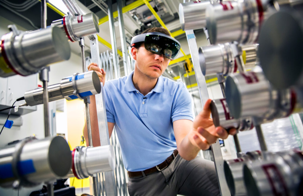 A man with a headset over his eyes crouches down among round metal devices.