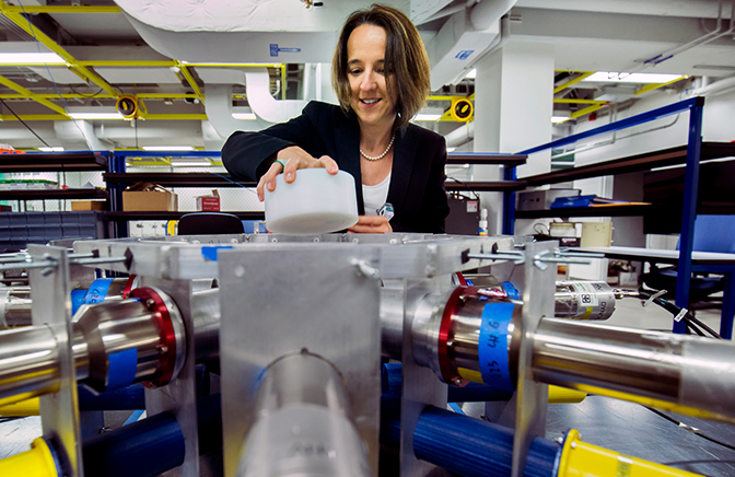 A woman placing a cylinder in a large device in a lab.