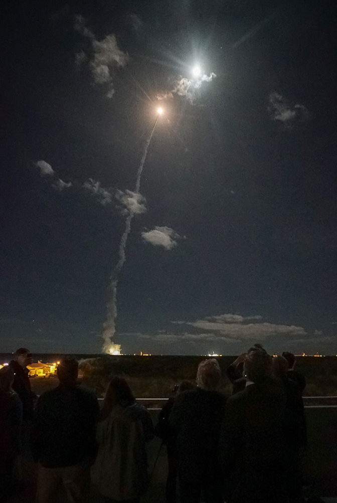 A bright light shooting into the night sky, leaving a trail of smoke.