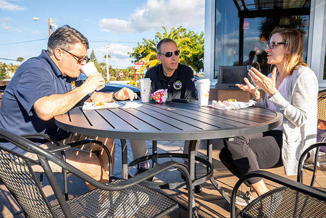 Three people seated around a table eating food.