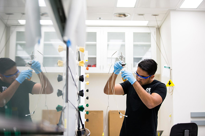 A man in safety goggles holding up a container with tubes coming out of it.