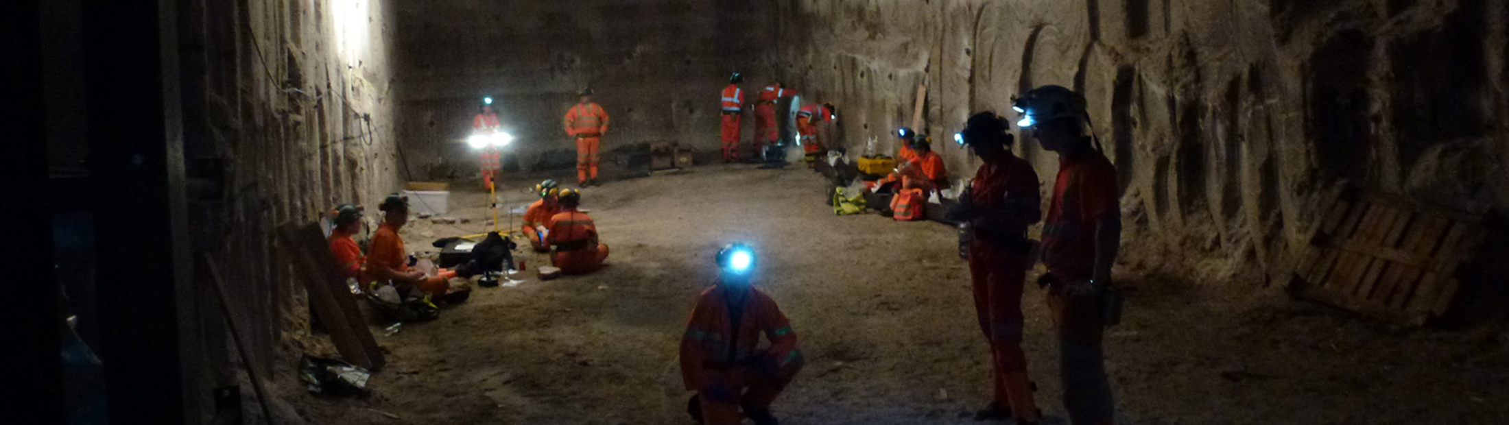 Several people in orange jumpsuits and hardhats in an underground tunnel.