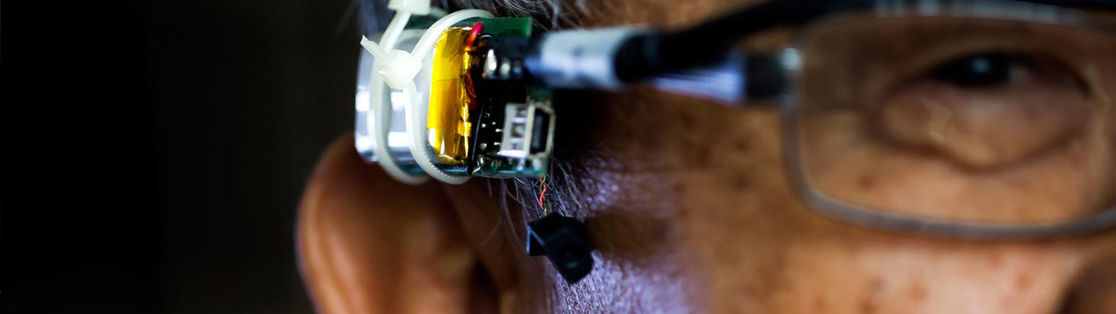 Close up of a man with glasses, attached is the wearable security device