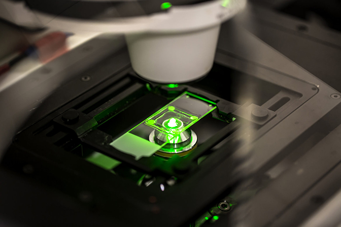 A microscope lens shining a green light on a glass slide.