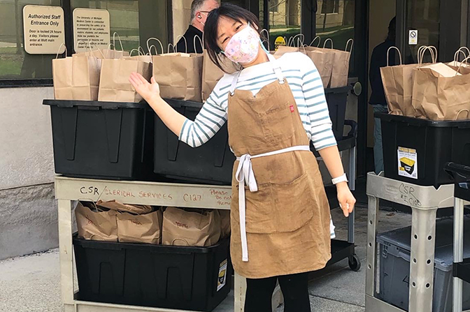 A woman in a face mask gestures to carts full of paper bags.