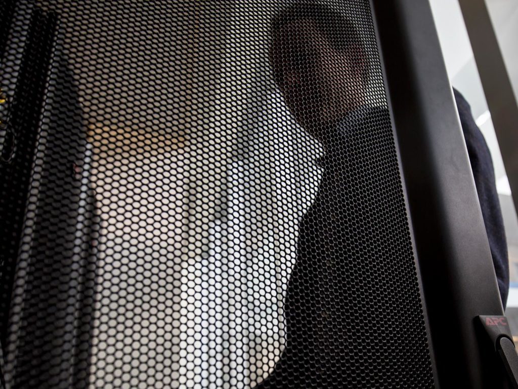 A man looking behind a mesh screen.