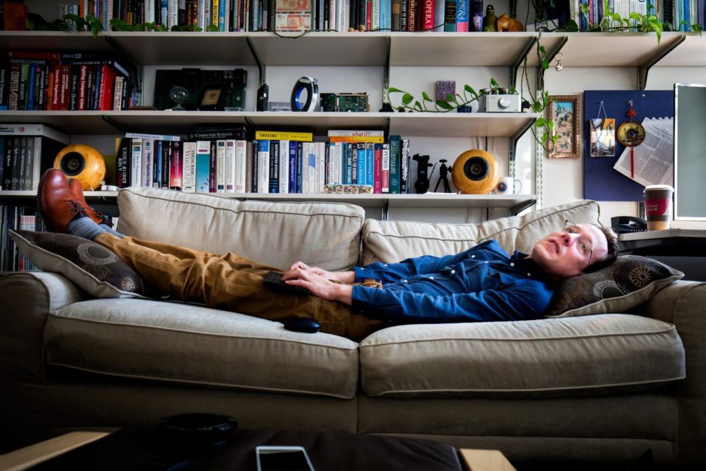 A man lying on a futon with many bookshelfs behind him.