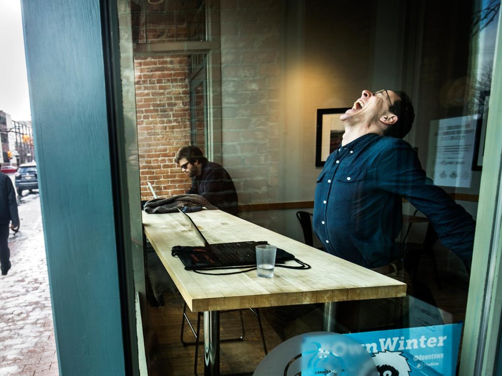 A man stretching at a table by a window.