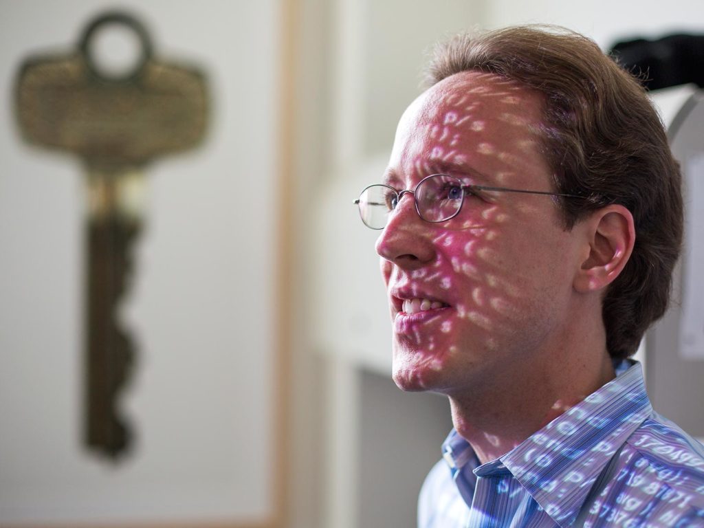 A man in front of a projecter displaying code over his face.