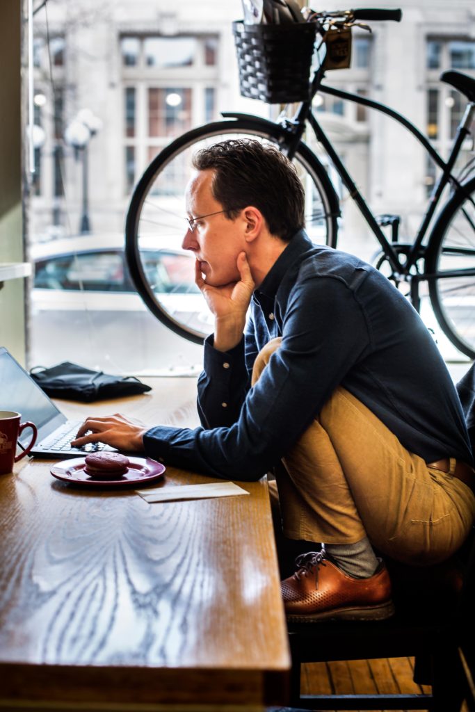 A man sitting in a coffee shop working on a laptop.