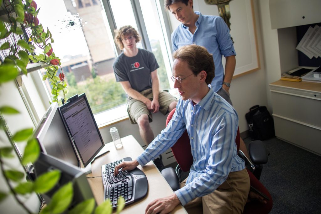 Three men in an office looking at a computer screen.