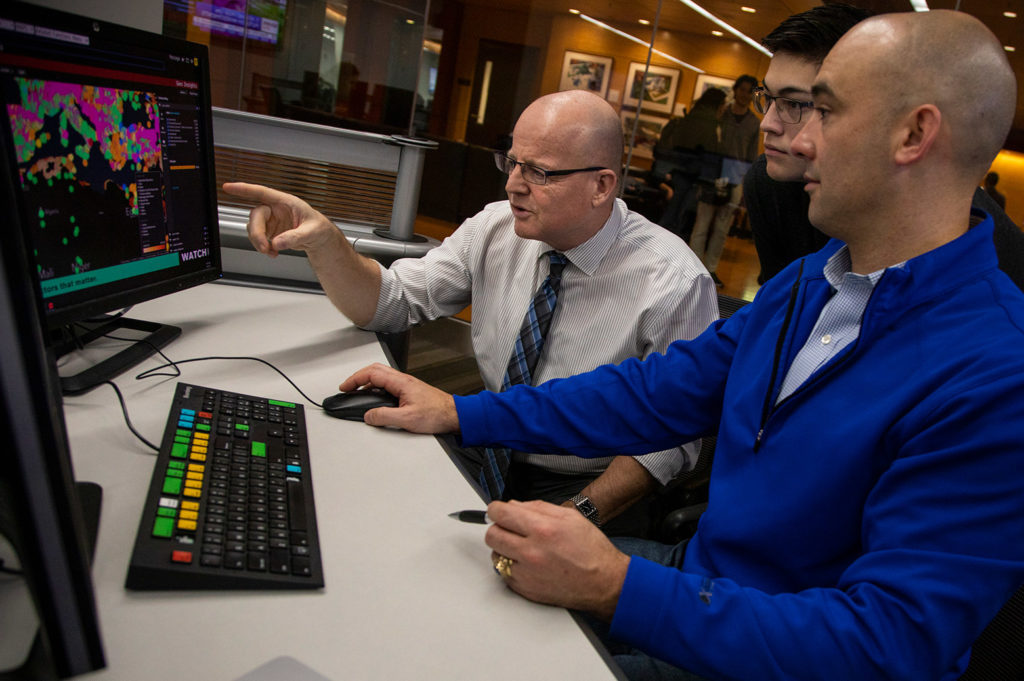 One man gesturing at a computer screen while two men watch.