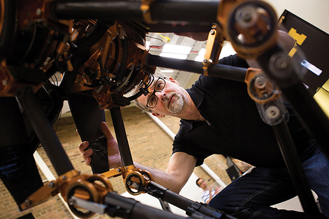 A man crouching by a large robot.