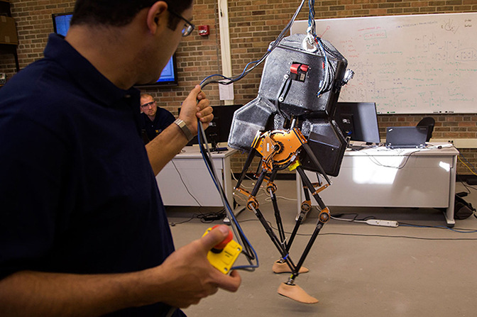 A man holding wires connected to a robot.