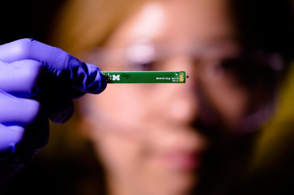 A person holds up a small, thin, green device to the camera.