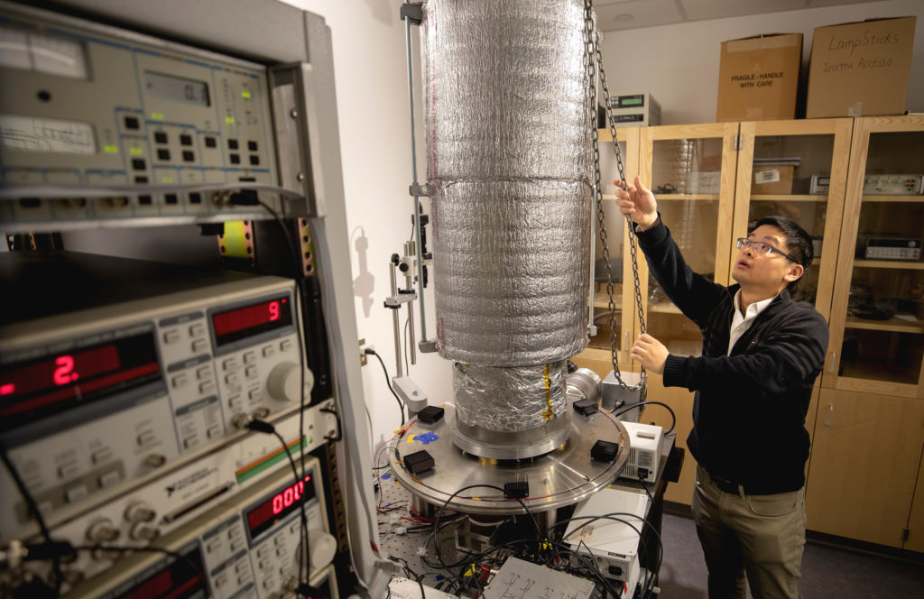 A man adjusts a large cylindriccal device surrounded by electrical equipment.