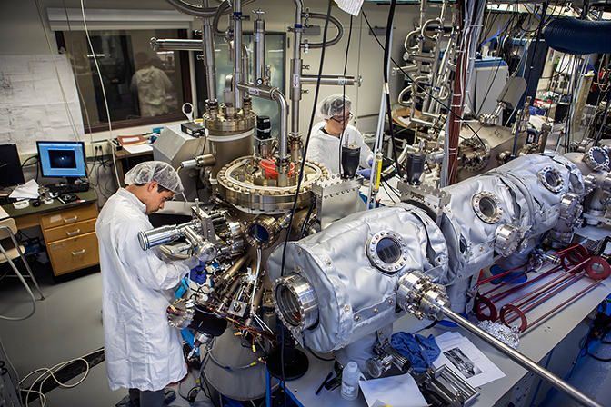 Two researchers in a lab working on a very large metal apparatus.