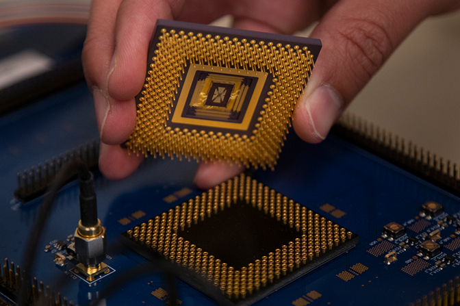 A hand holding a small sqaure device above a circuit.