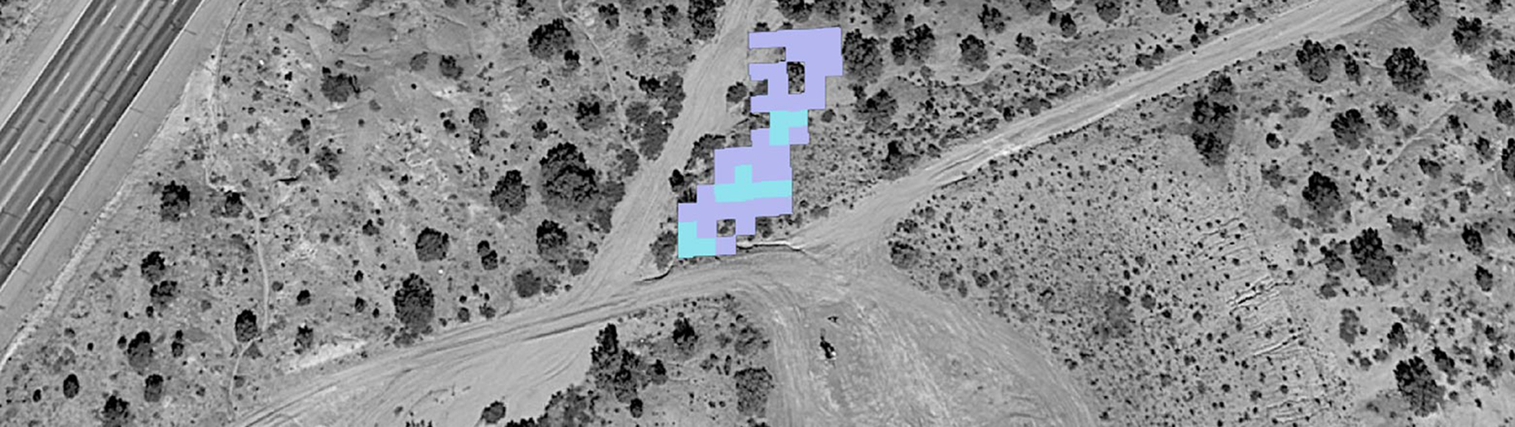 An aerial view of the ground in grayscale and a pixelated purple and blue area in the center.