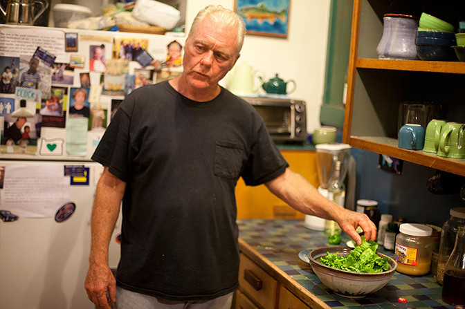 A man putting lettuce into a bowl on a kitchen counter.