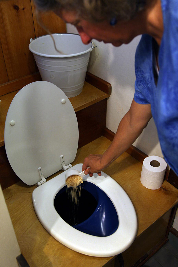 A woman pouring a cup of wood shavings into a toilet.