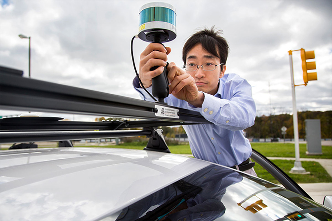 Image of Ding Zhao adjusting a LIDAR system on test vehicle at Mcity