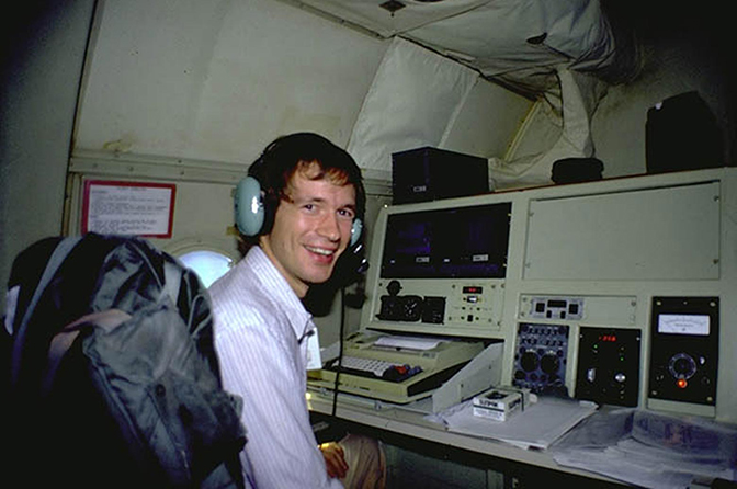 A man wearing headphones sitting at a control panel with many knobs and buttons.