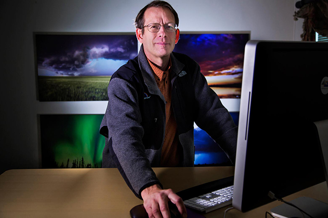 A man using a desktop computer while facing the camera and smiling.