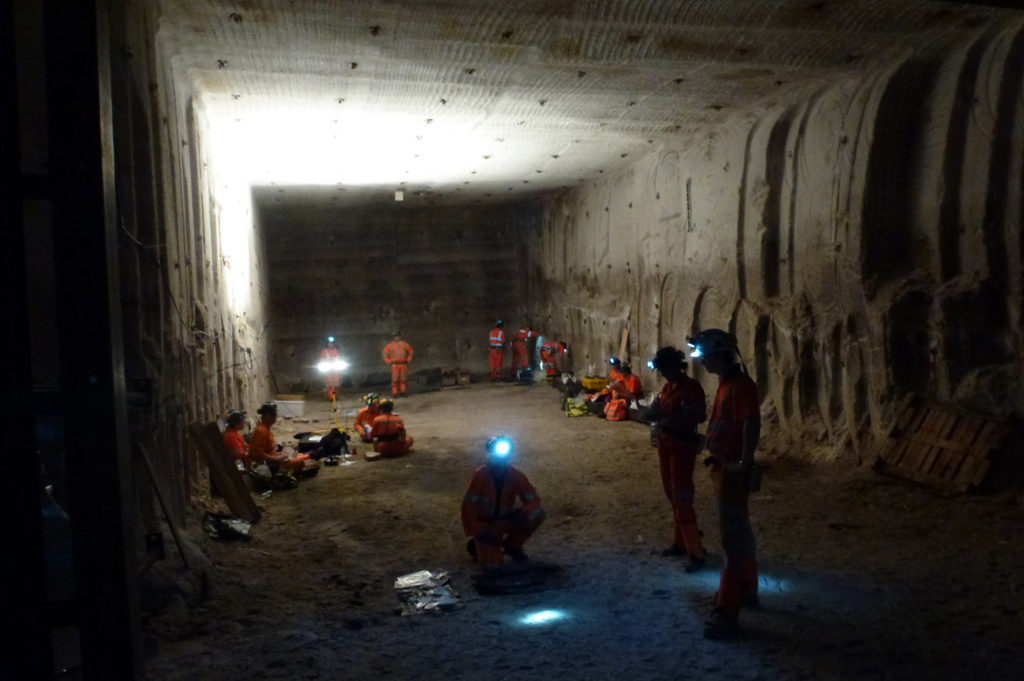 Several people in orange jumpsuits and hardhats in an underground tunnel.