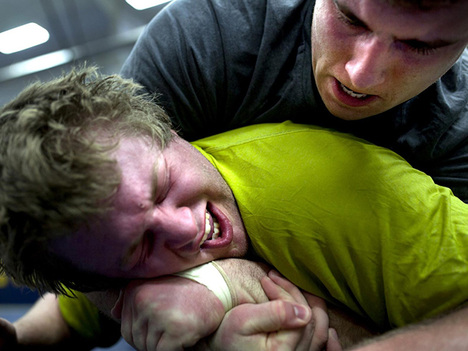 Two people wrestling, one of whom is held in a chokehold by the other.