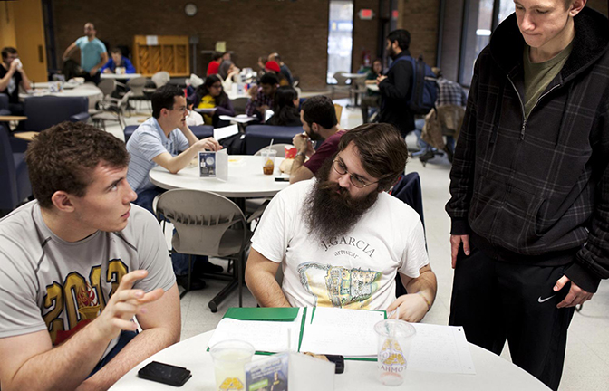 Three people talking at a round table while writing on paper.