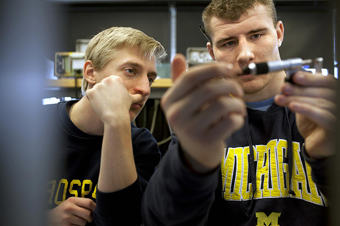 Two people with Michigan apparel looking at a small device.