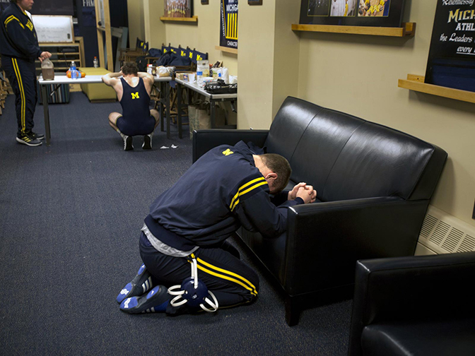 A person crouching beside a couch with their hands together.