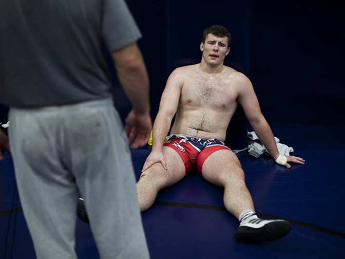 A person in wrestling gear sitting on the ground clutching their leg.