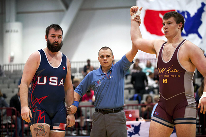 A wrestling referee holding two wrestlers hands, one of them held in the air in victory.